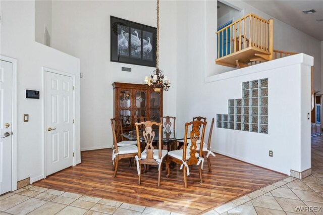 dining space featuring baseboards, visible vents, a towering ceiling, tile patterned floors, and a chandelier