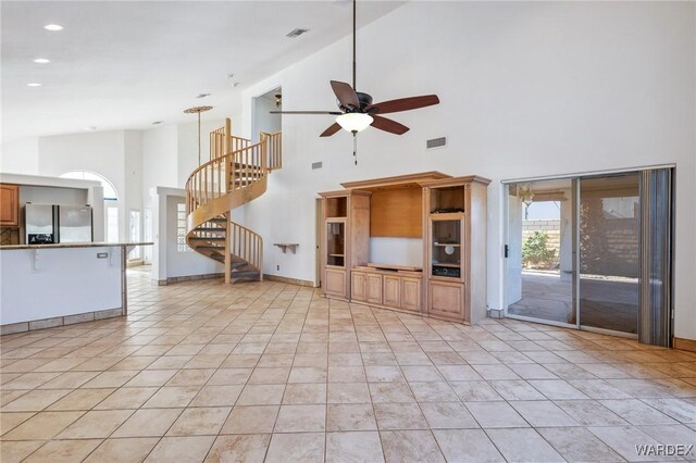 unfurnished living room with visible vents, ceiling fan, stairway, high vaulted ceiling, and light tile patterned flooring