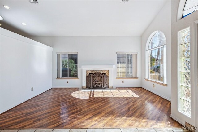 unfurnished living room with lofted ceiling, recessed lighting, wood finished floors, a fireplace with flush hearth, and baseboards