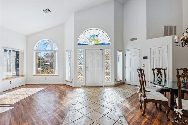 foyer featuring vaulted ceiling, light wood-type flooring, visible vents, and an inviting chandelier