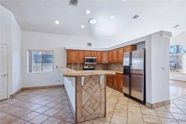 kitchen featuring visible vents, a breakfast bar area, brown cabinets, stainless steel appliances, and light countertops