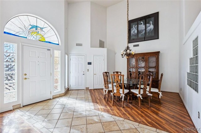 entrance foyer featuring a chandelier, light wood finished floors, a towering ceiling, and visible vents