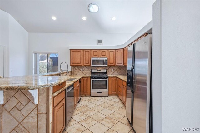 kitchen featuring brown cabinets, tasteful backsplash, appliances with stainless steel finishes, a sink, and a peninsula