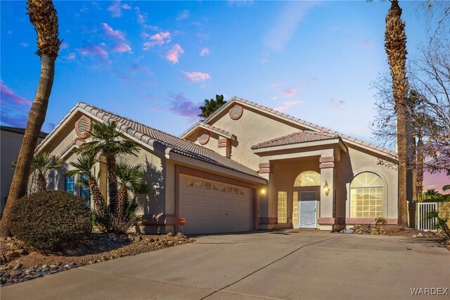 mediterranean / spanish house with a tile roof, driveway, an attached garage, and stucco siding