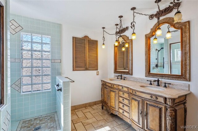 bathroom with double vanity, tiled shower, a sink, and baseboards