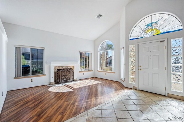 entrance foyer featuring light tile patterned floors, visible vents, a fireplace with flush hearth, high vaulted ceiling, and baseboards