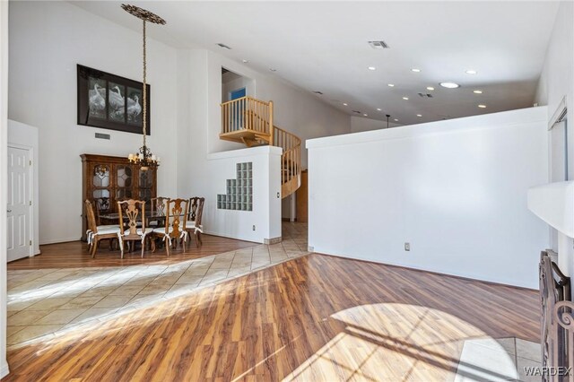 living area with visible vents, an inviting chandelier, a towering ceiling, and light wood-style floors