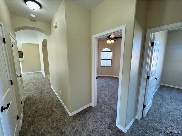 corridor with arched walkways, dark carpet, and baseboards