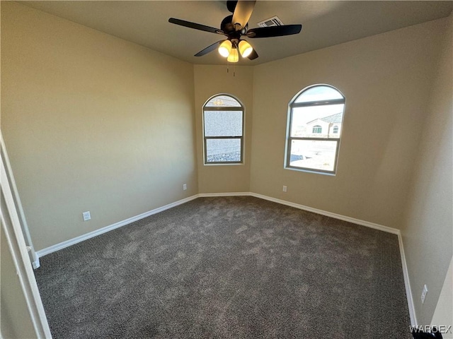 spare room featuring visible vents, dark carpet, baseboards, and ceiling fan