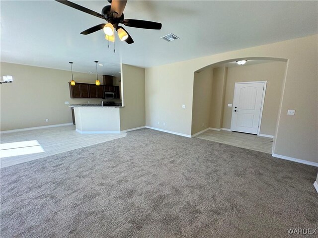 unfurnished living room featuring arched walkways, visible vents, a ceiling fan, light carpet, and baseboards