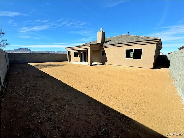 back of property with a patio, a fenced backyard, a mountain view, stucco siding, and a chimney