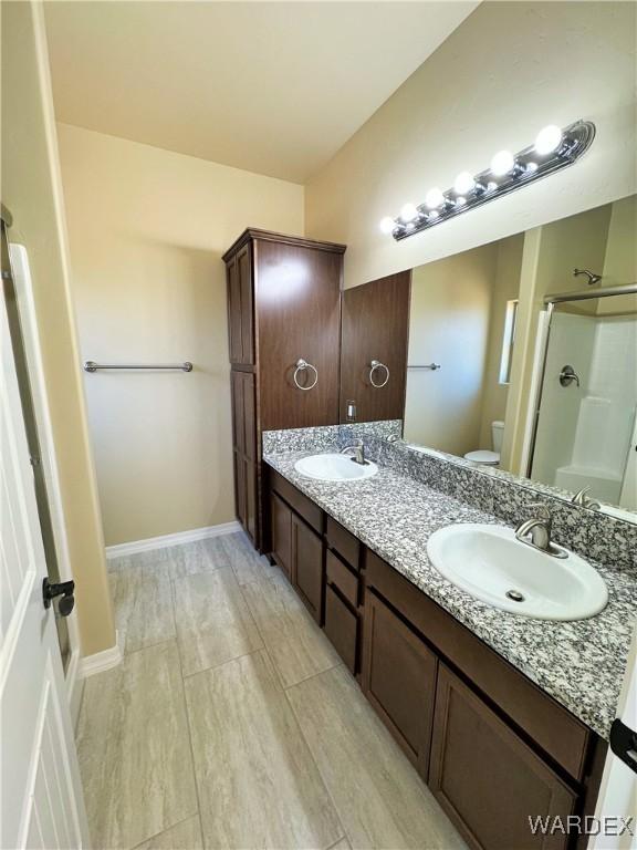 bathroom with double vanity, walk in shower, a sink, and toilet