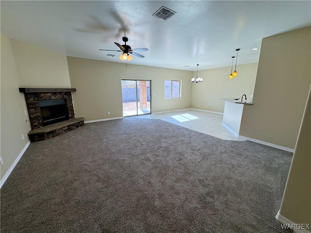 unfurnished living room with visible vents, carpet flooring, a stone fireplace, baseboards, and ceiling fan with notable chandelier