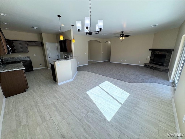 kitchen featuring dark brown cabinetry, open floor plan, decorative light fixtures, light stone countertops, and a stone fireplace