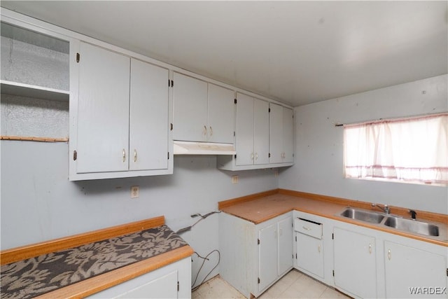 kitchen with under cabinet range hood, white cabinetry, light countertops, and a sink