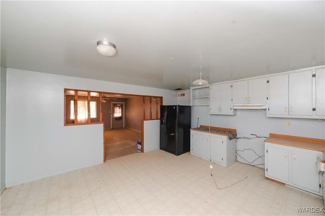 kitchen featuring light floors, a ceiling fan, white cabinets, and black fridge