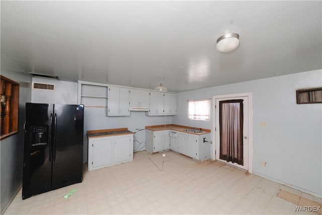 kitchen with visible vents, black fridge, light floors, white cabinetry, and a sink