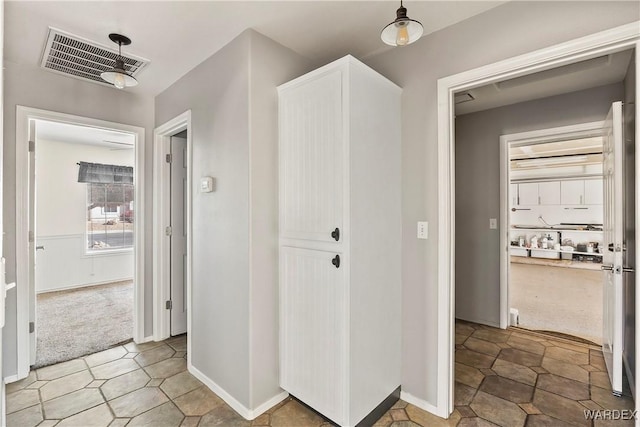 hall featuring baseboards, visible vents, and carpet flooring