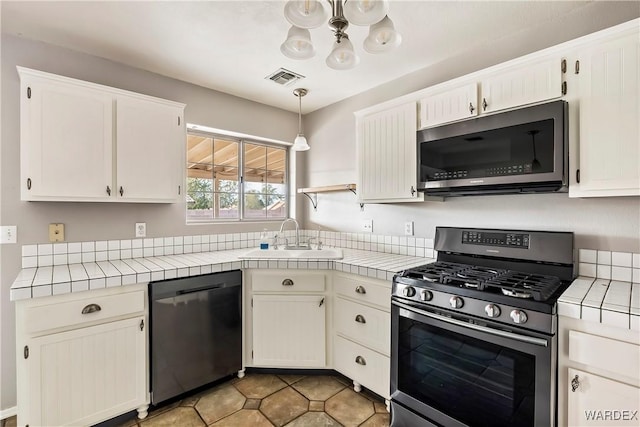 kitchen with tile countertops, stainless steel appliances, a sink, and hanging light fixtures