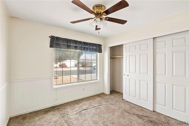 unfurnished bedroom featuring a wainscoted wall, a closet, carpet flooring, and a ceiling fan