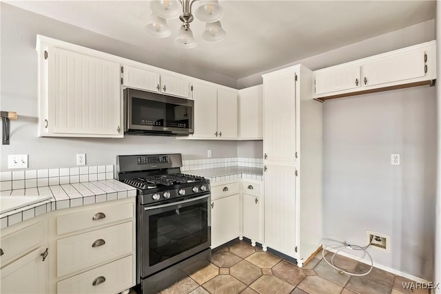 kitchen with stainless steel appliances, tile counters, a notable chandelier, and light tile patterned floors