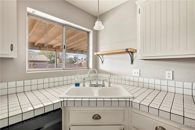 kitchen with decorative light fixtures, open shelves, tile counters, white cabinetry, and a sink