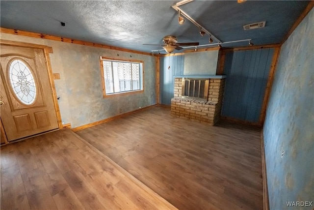 unfurnished living room with visible vents, a brick fireplace, ceiling fan, wood finished floors, and baseboards