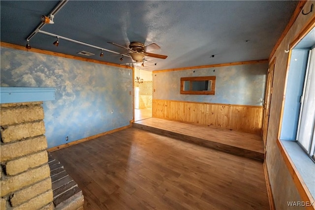 unfurnished living room featuring visible vents, a ceiling fan, wainscoting, wooden walls, and wood finished floors