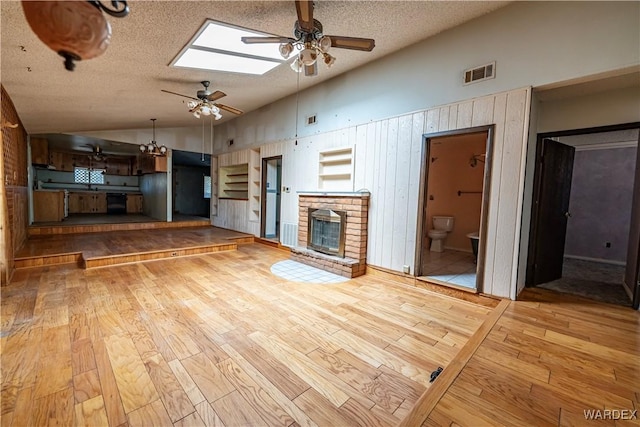 unfurnished living room with a skylight, visible vents, a textured ceiling, light wood-type flooring, and a fireplace