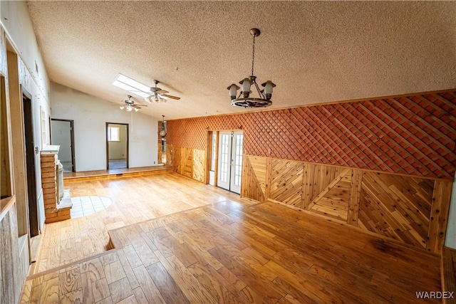 spare room featuring light wood finished floors, lofted ceiling, a healthy amount of sunlight, a textured ceiling, and ceiling fan with notable chandelier