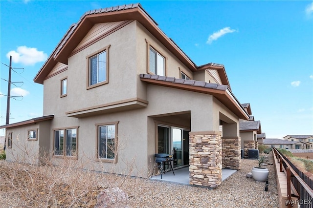 back of house with a patio, central AC, fence, stone siding, and stucco siding