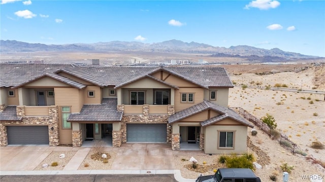 view of front of property with an attached garage, stone siding, a mountain view, and concrete driveway