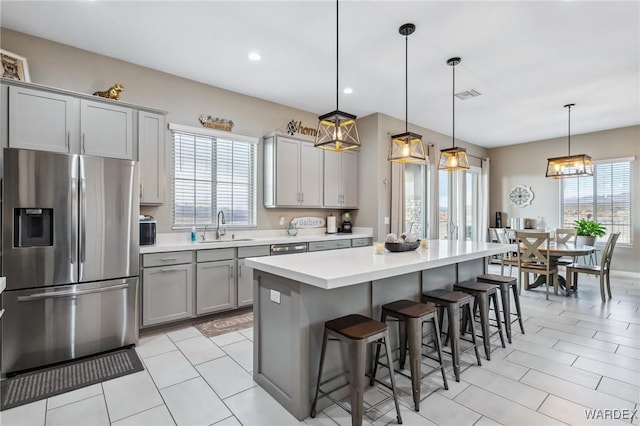 kitchen featuring stainless steel fridge with ice dispenser, a breakfast bar, hanging light fixtures, light countertops, and a sink