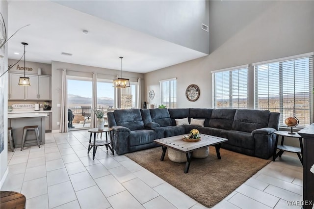 living area with light tile patterned floors, a high ceiling, visible vents, and an inviting chandelier