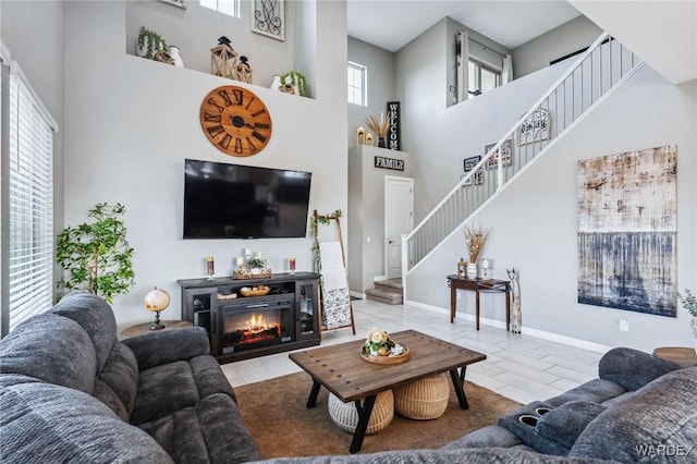 living room featuring stairs, a high ceiling, a glass covered fireplace, and baseboards