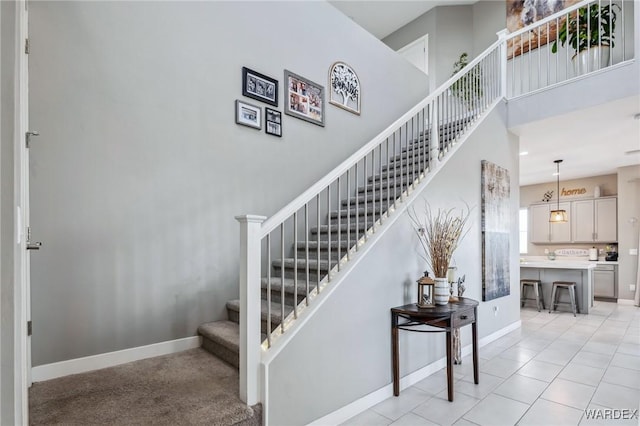 stairway featuring a towering ceiling, baseboards, and tile patterned floors