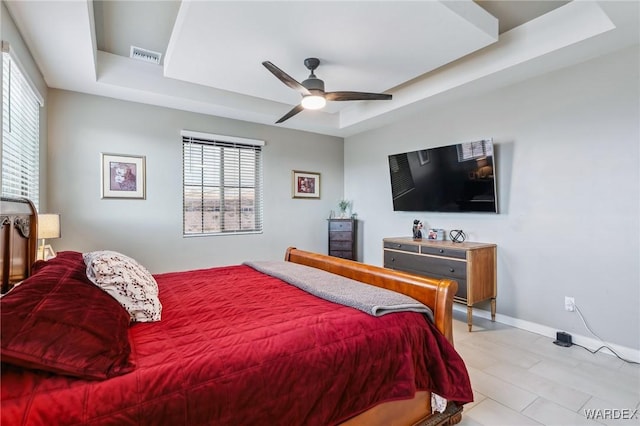 bedroom with ceiling fan, a tray ceiling, visible vents, and baseboards