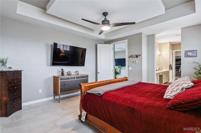 bedroom with a raised ceiling, ceiling fan, ensuite bath, and baseboards