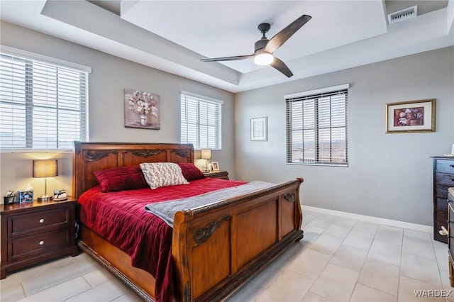 bedroom with ceiling fan, a tray ceiling, visible vents, and baseboards