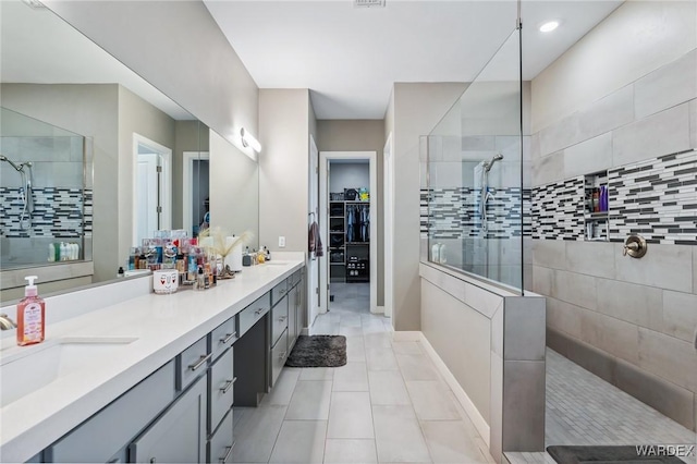 bathroom with double vanity, a spacious closet, a sink, tile patterned flooring, and walk in shower