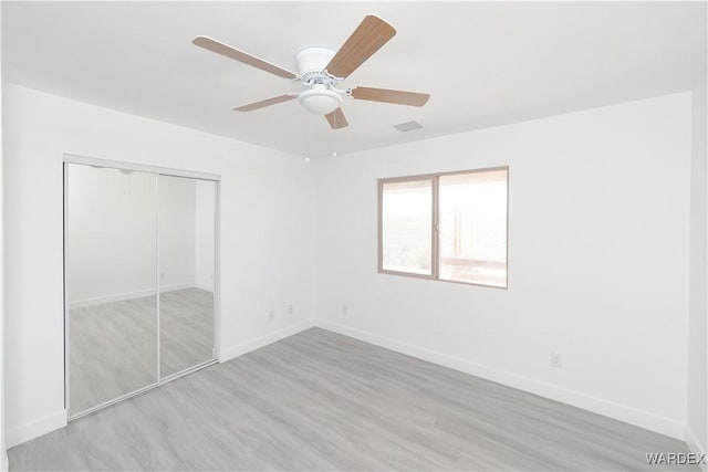 unfurnished bedroom featuring light wood finished floors, a closet, visible vents, a ceiling fan, and baseboards