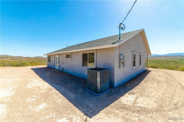 back of house with roof with shingles, central AC, and stucco siding