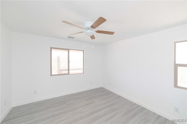 empty room featuring a healthy amount of sunlight, visible vents, light wood-style flooring, and baseboards