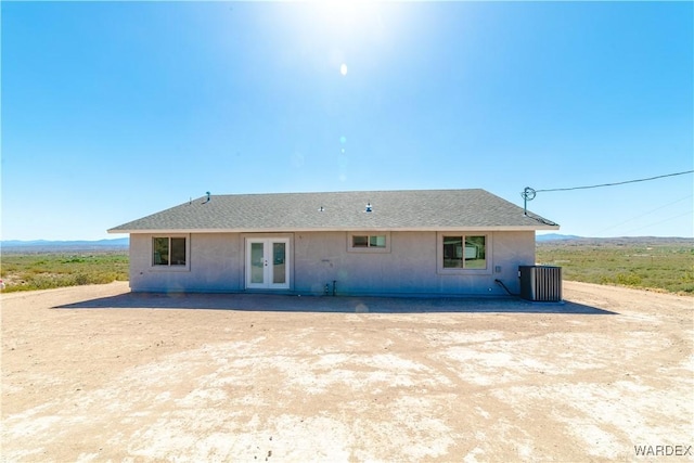 rear view of property featuring stucco siding, roof with shingles, central AC unit, and french doors