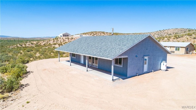 exterior space with roof with shingles, a mountain view, a patio, and stucco siding