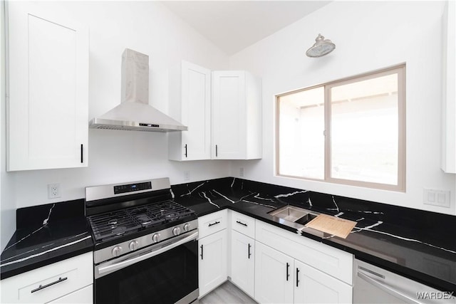 kitchen featuring wall chimney range hood, dark countertops, appliances with stainless steel finishes, and white cabinets