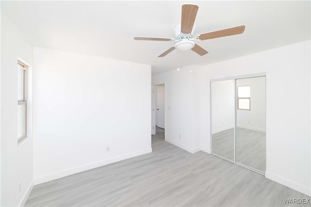 unfurnished bedroom featuring baseboards, ceiling fan, a closet, and light wood-style floors