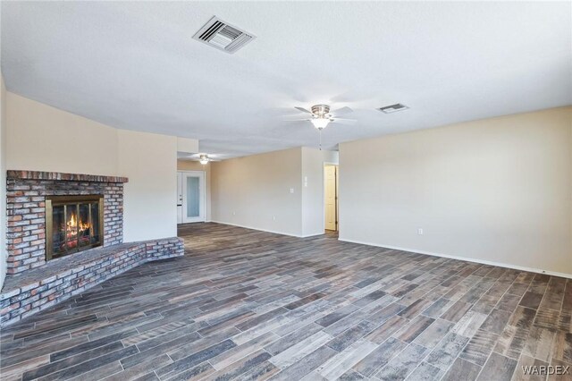 unfurnished living room with a brick fireplace, ceiling fan, visible vents, and dark wood-style flooring