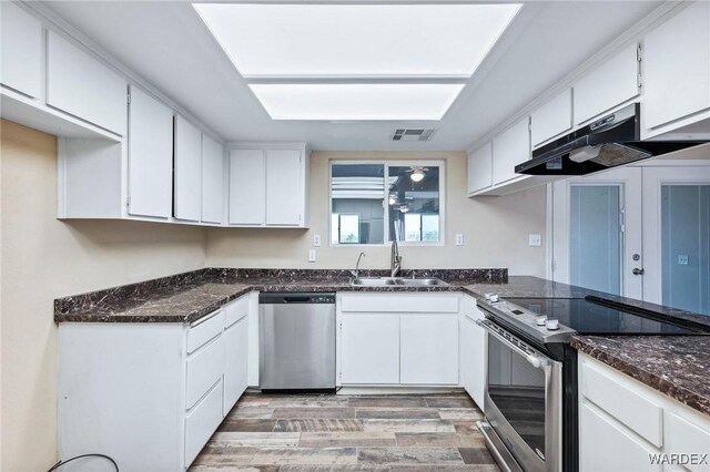 kitchen featuring white cabinets, light wood-style floors, stainless steel appliances, under cabinet range hood, and a sink