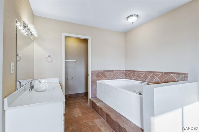 full bath featuring stone tile floors, baseboards, a bath, and vanity